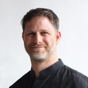 Portrait of Brad Samuels who has short hair, a short beard and is wearing a black shirt in front of a white background.