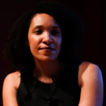 Color portrait of Jasmine Nichole Cobb. She has short, dark hair and smiles softly against a black backdrop.