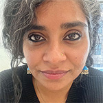 A person with curly hair wearing blue and gold earrings and a black shirt.