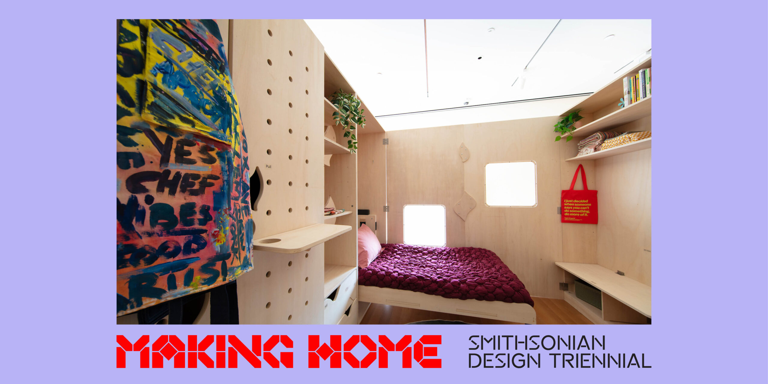 A small room made of light colored wood. The back wall has two small windows. The bed has a dark pink quilt and pink pillow, and is in the far left corner. Various shelves line the far right wall. A colorful textile is visible on the left of the image. A light purple border surrounds the image, with the words Making Home: Smithsonian Design Triennial at the bottom.