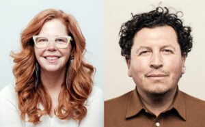 A smiling woman with long red hair wearing light framed glasses on the left. A man with short dark hair wearing a brown collared shirt on the right.