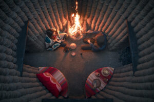 Birds eye view of two people enjoying cooking with tagines over a campfire within a small walled-in space.