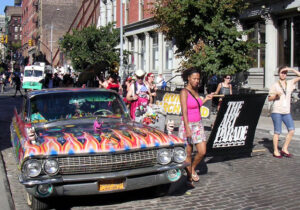 Photograph of people marching in a street carrying a large banner that reads [The Art Parade].