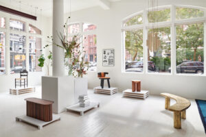 A white gallery wall interior with several pieces of furniture displayed on elevated pedestals arranged in a semi-circle around a central column.