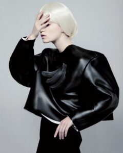 A model wears a sleek black oversized jacket with a sculpture of life-sized black-colored bananas on the front torso.