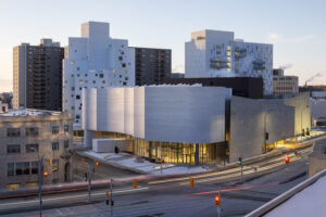 A curved and undulating facade of an ultra modern stone and glass building on a city street.