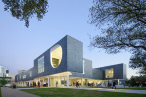 The facade of an ultra modern boxy dark grey building on stilts.