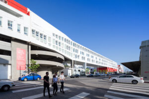 Facade of a modern white building elevated on columns that undulates as it stretches down a city street.