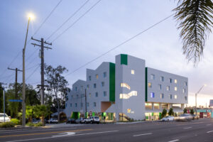 Facade of a modern white building at dusk with an undulating triangular roof and decorated with accents of dark green.