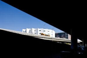 Photo of the top of a rounded and multi-sided building seen from a highway underpass.