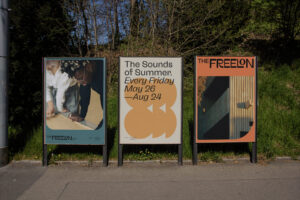 Three large stylized advertisement posters of Freelon and the Sounds of Summer along a public walkway.