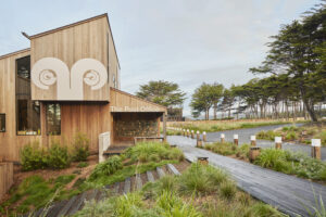 A large midcentury style wood-shingled building labeled [The Post Office] set on a sloping hill with manicured grass and tree-lined pathways.